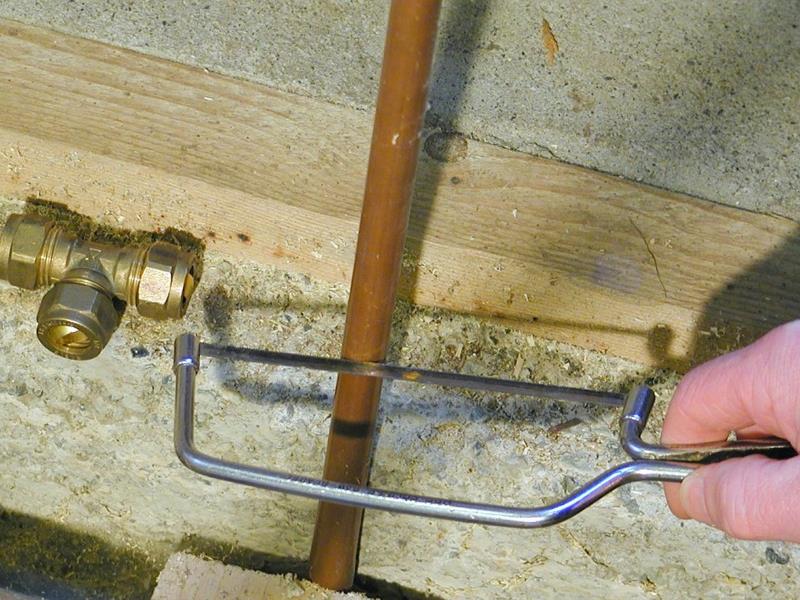 A hacksaw in use, cutting copper pipes.
